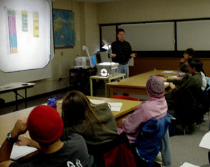 Cam asks his class a question about a geologic timeline shown on an overhead